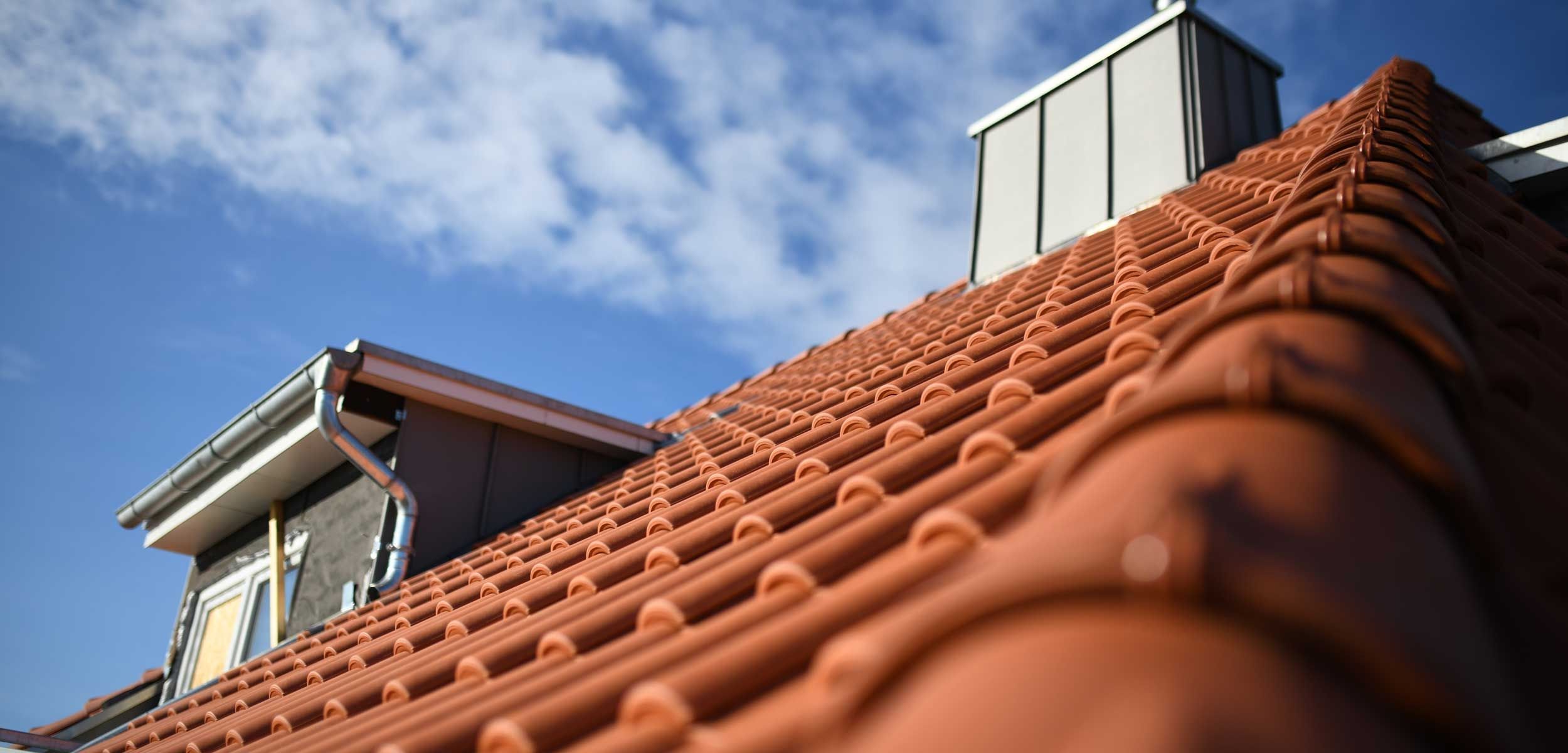 Rotes Satteldach mit Dachziegel, Metallrinne und Dachfenster gegen blauen Himmel